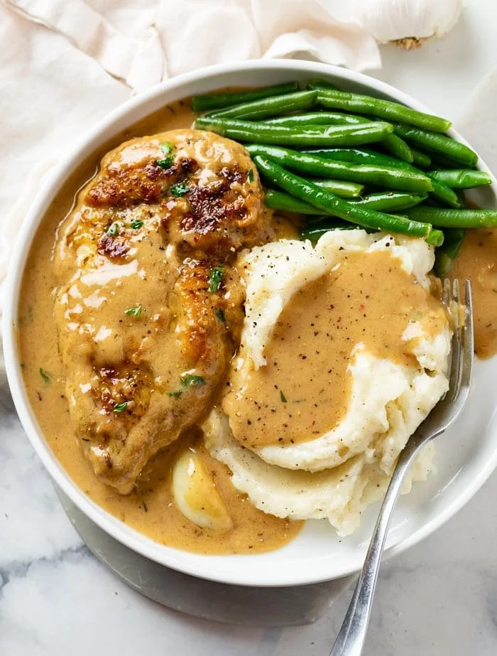 Creamy garlic chicken served on a plate with herbs and vegetables