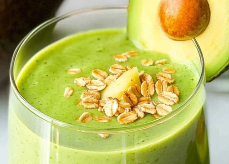 Delicious avocado smoothie in a glass with ingredients on a wooden table.