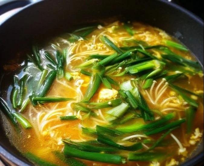 Bowl of Enoki Mushroom Soup garnished with green onions and herbs