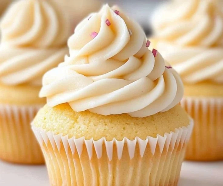 Delicious vanilla cupcakes topped with creamy frosting on a decorative plate.