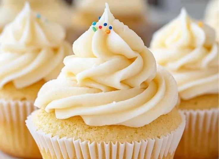 Delicious vanilla cupcakes with creamy frosting topped with sprinkles.