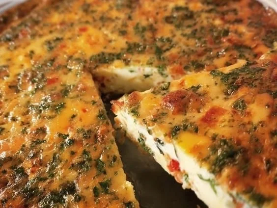 A slice of crustless egg white quiche with fresh vegetables and herbs on a plate.