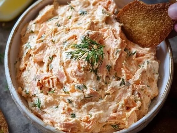 Creamy smoked salmon dip served in a bowl with crackers and herbs