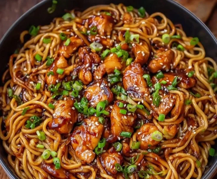 Sticky garlic chicken noodles garnished with fresh herbs and vegetables